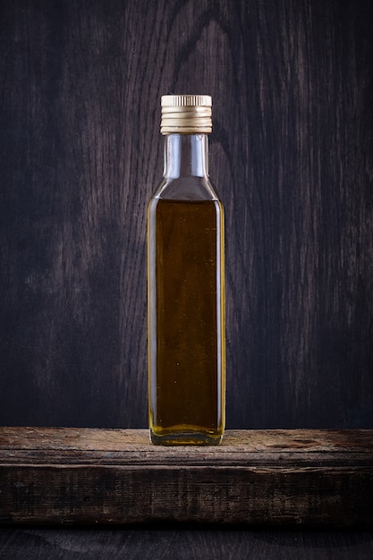 Transparent bottle filled with olive oil on dark backgrou