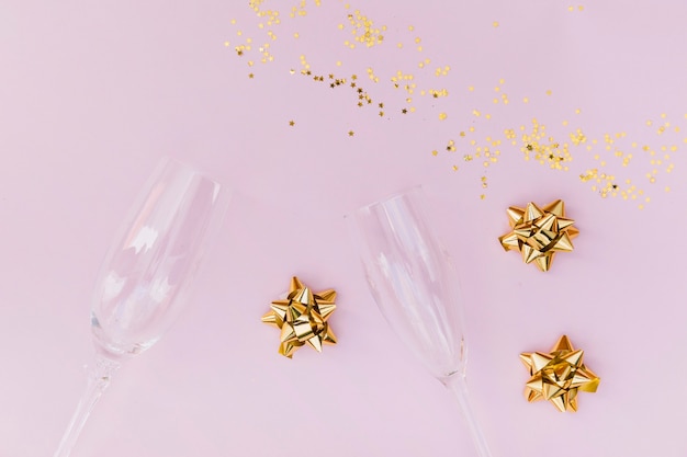 Transparent champagne glasses; golden bow and confetti on pink background