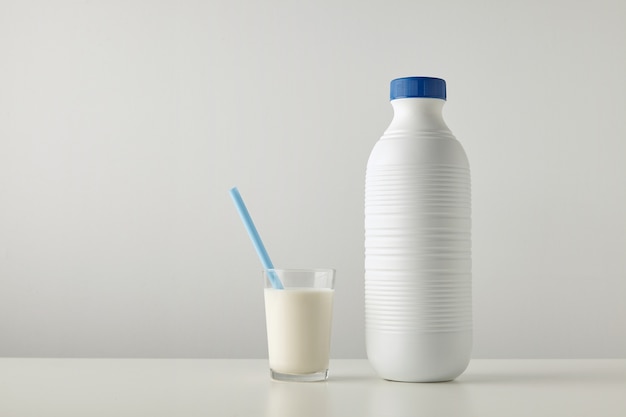 Transparent glass with fresh milk and blue drinking straw inside near plastic riffled blank bottle with blue cap