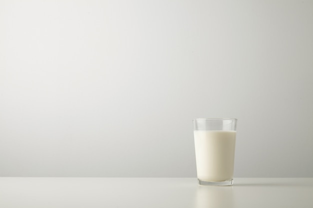 Transparent glass with fresh organic milk isolated on side of white table. Space for your text above