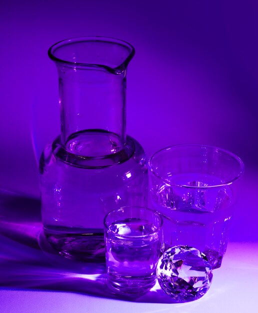 Прозрачные стаканы с водой; бриллиант и мензурка на фиолетовом фоне