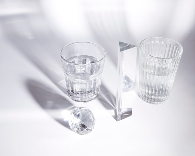 Transparent glasses of water; diamond and prism on white background with shadow