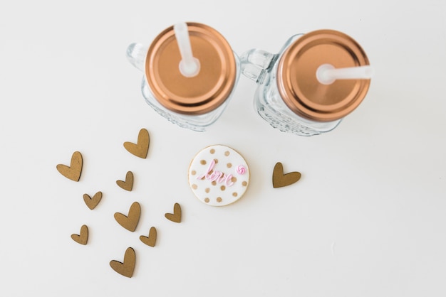 Transparent mason jar with love cookie and heart shapes on white backdrop