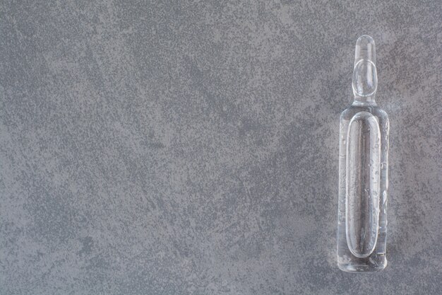 Transparent medical ampoule on marble table.