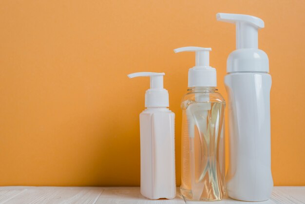 Transparent and white soap dispenser bottles against an orange background