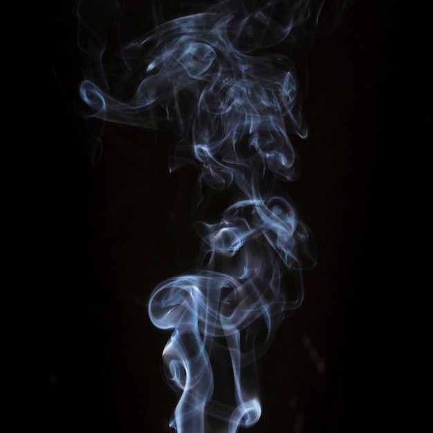 黒の暗い背景に対して透明な白い渦巻き煙