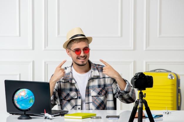 赤い眼鏡をかけているカメラで旅行vlogを記録する麦わら帽子の若いハンサムな男で旅行ブロガー