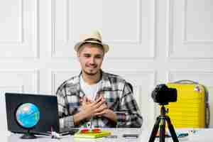 Free photo travel blogger in straw hat young handsome guy recording trip vlog on camera holding chest