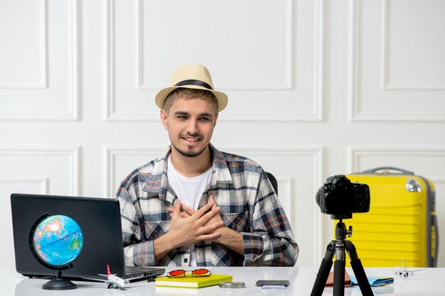 Travel blogger in straw hat young handsome guy recording trip vlog on camera holding chest