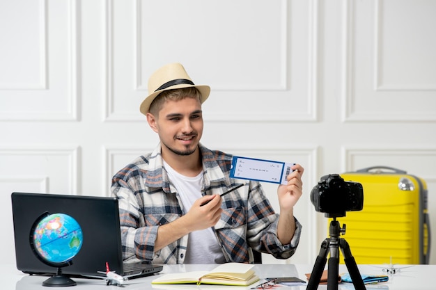 Travel blogger wearing straw hat young handsome guy recording trip vlog on camera holding ticket
