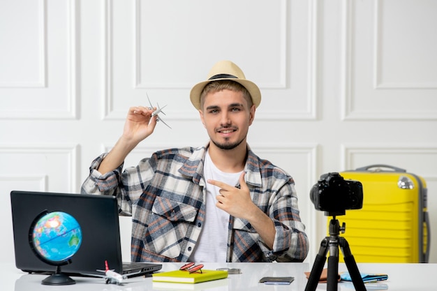 Free photo travel blogger wearing straw hat young handsome guy recording trip vlog on camera with tiny plane