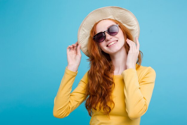 Travel concept - Close up Portrait young beautiful attractive redhair girl wtih trendy hat and sunglass smiling. Blue Pastel Background. Copy space.