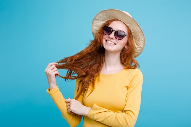 Travel concept - Close up Portrait young beautiful attractive redhair girl wtih trendy hat and sunglass smiling. Blue Pastel Background. Copy space.