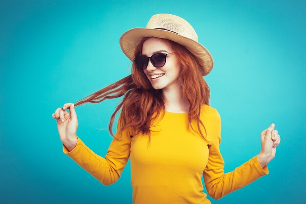 旅行の概念 - クローズアップ肖像画若い美しい魅力的な赤毛の女の子と流行の帽子とサングラス笑顔。青いパステルの背景。スペースをコピーします。