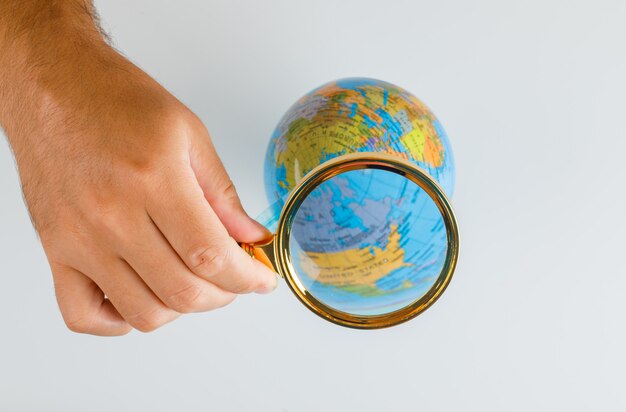 Travel concept flat lay. hand holding magnifying glass over globe.