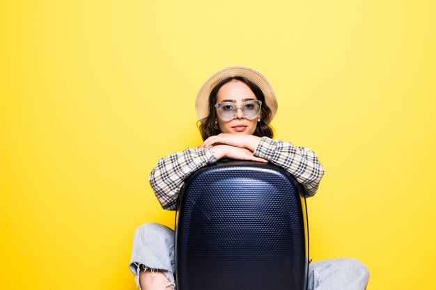 Travel Concept. Happy tourist woman with sunglasses and hat wearing jean clothes ready for travel hug suitcase isolated.