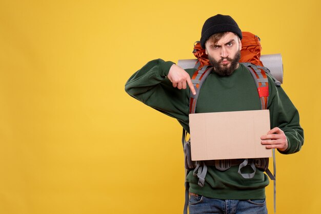 Travel concept with confident young guy with packpack and pointing free space for writing on yellow 