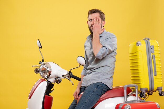 Free photo travel concept with emotional nervous young man sitting on motocycle with suitcases on it on yellow