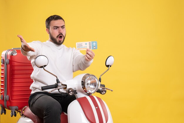 Travel concept with nervous man sitting on motorcycle with suitcase on it showing ticket on yellow