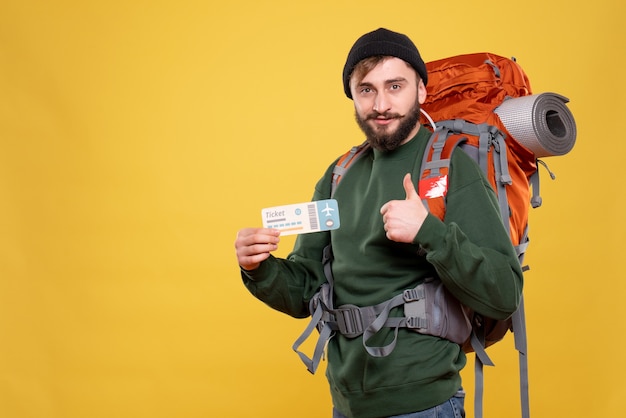 Packpack과 함께 웃는 젊은 남자와 노란색에 확인 제스처를 만드는 티켓을 들고 여행 개념