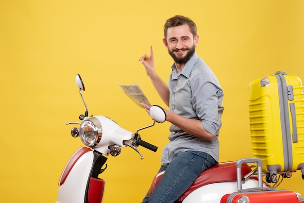 Travel concept with smiling young man sitting on motocycle with suitcases on it and holding map on yellow