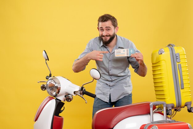 Travel concept with smiling young man standing behind motocycle with suitcases on it and holding ticket on yellow 