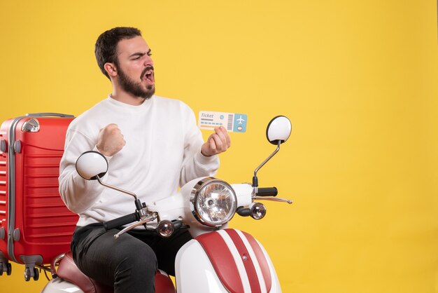 Travel concept with surprised man sitting on motorcycle with suitcase on it showing ticket on yellow