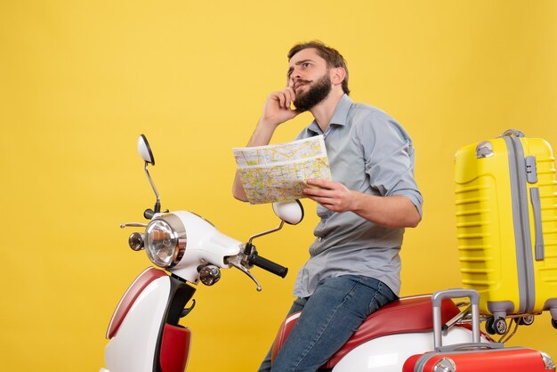 スーツケースを持ってバイクに座って、黄色の地図を保持している若い男を考えて旅行の概念