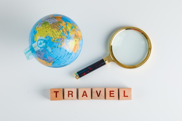 Travel concept with wooden cubes, magnifying glass, globe flat lay.