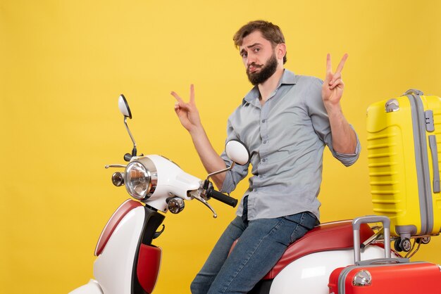 Travel concept with young emotional bearded man sitting on motocycle on it making victory gesture on yellow 