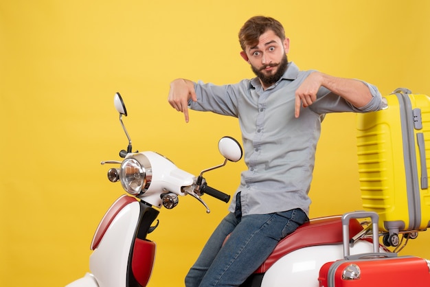 Free photo travel concept with young emotional bearded man sitting on motocycle on it pointing down on yellow