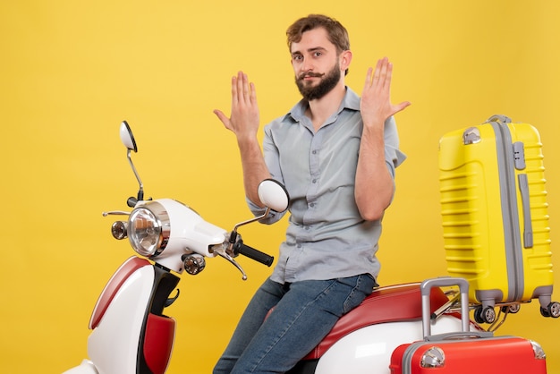 Travel concept with young emotional bearded man sitting on motocycle on it showing hands on yellow 