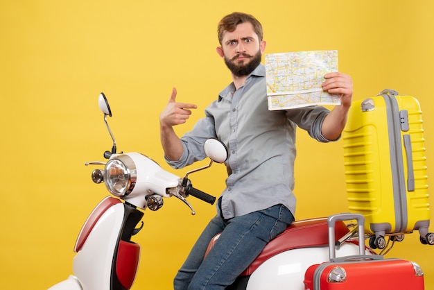 若い感情的なひげを生やした男がオートバイに座って、黄色でその上に前向きの地図を指している旅行の概念