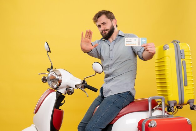 若い感情的なひげを生やした男がオートバイに座って、黄色の5つの保持チケットを示す旅行の概念