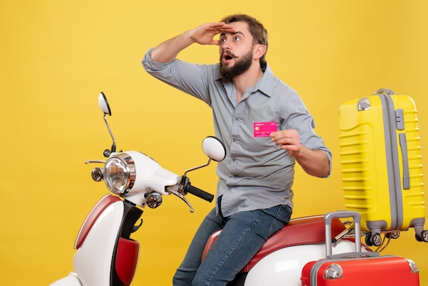 Concetto di viaggio con giovane uomo barbuto concentrato emotivo che si siede sulla motocicletta e che tiene la carta di credito su di esso su giallo