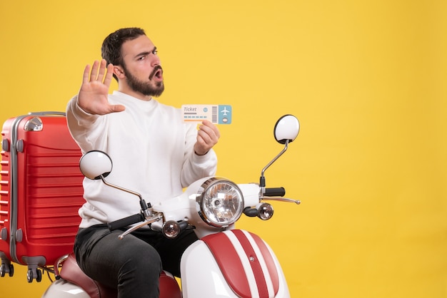 Концепция путешествия с молодым эмоциональным человеком, сидящим на мотоцикле с чемоданом на нем, показывая билет на желтом