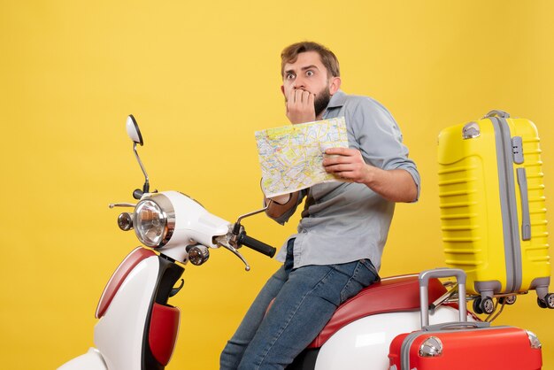 Travel concept with young scared bearded man sitting on motocycle and showing map on it on yellow 