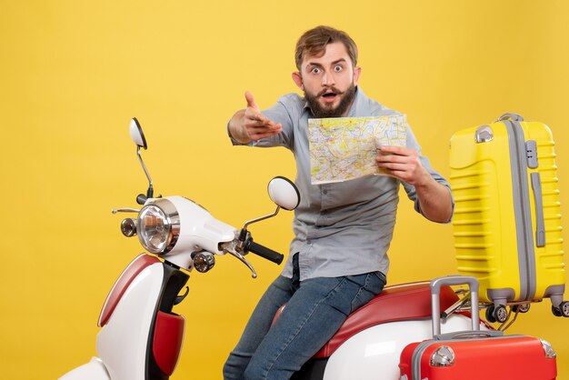 Travel concept with young wondering bearded man sitting on motocycle and showing map on it on yellow 