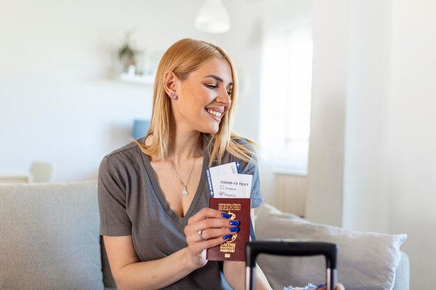 Travel during covid19 pandemic smiling woman with passport air tickets and covid passport at modern home in sunny day