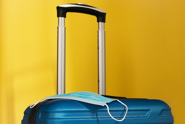 Covid​-​19​の​期間中​に​旅行します​。​黄色​の​背景​に​医療用​マスク​と​スーツケース​。​休暇​、​コロナ​時代​の​休日​。​カラフル​な​デザイン​。