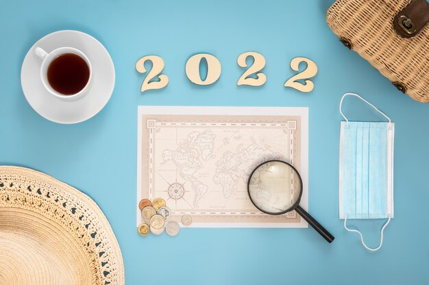 Free photo travel flat lay composition with world map and numbers 2022 on blue background.