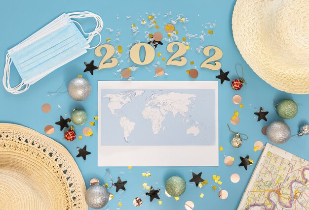 Travel flat lay composition with world map and numbers 2022 on blue background.