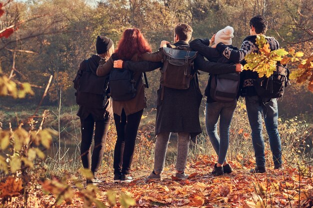 여행, 하이킹, 모험 개념입니다. 함께 껴안고 아름다운 가을 숲의 호수를 바라보는 젊은 친구들의 뒷모습.