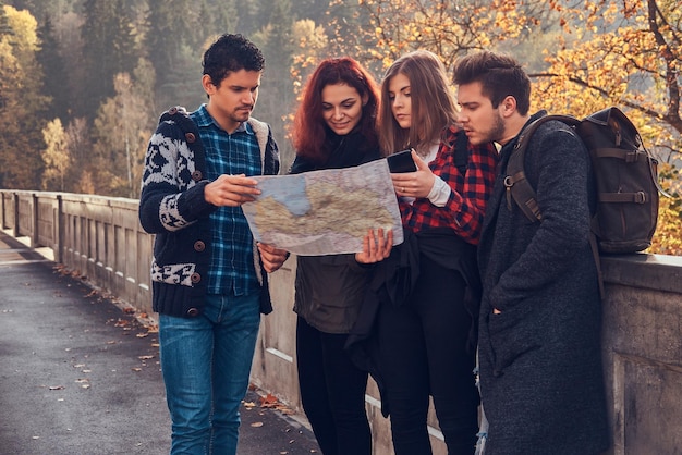 旅行、観光、ハイキング、人々のコンセプト。地図を見て、秋の森で旅行を計画している若い友人の写真。