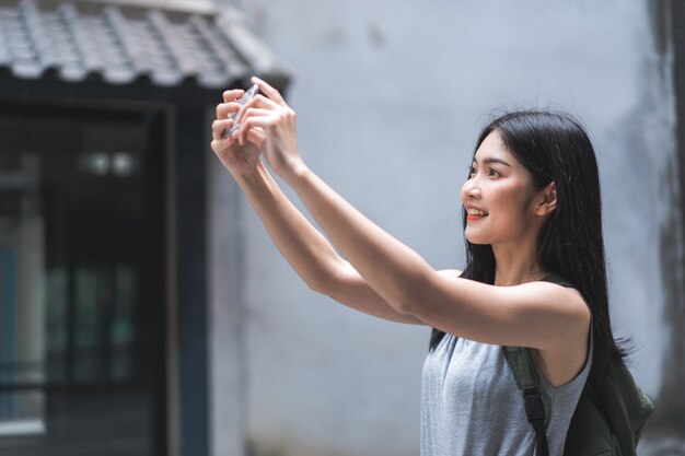 中国の北京で休暇旅行を過ごしながら写真を撮るために携帯電話を使用して旅行者アジア女性