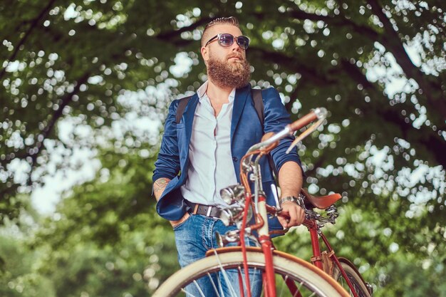 A traveler dressed in casual clothes and sunglasses with a backpack, relaxing in a city park after riding on a retro bicycle.