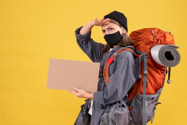 traveler girl with black mask and backpack holding cardboard observing