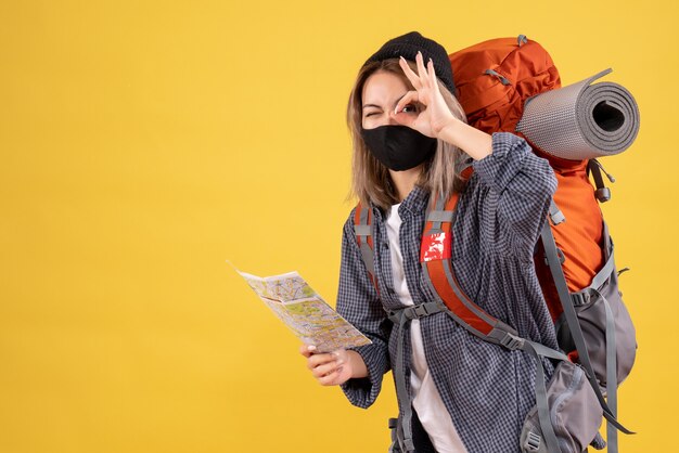 traveler girl with black mask and backpack holding map putting ok sign in front of her eye