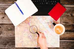 Free photo traveler holding magnifying glass over map besides coffee and diary on table