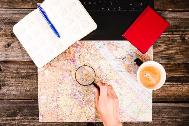 Traveler holding magnifying glass over map besides coffee and diary on table